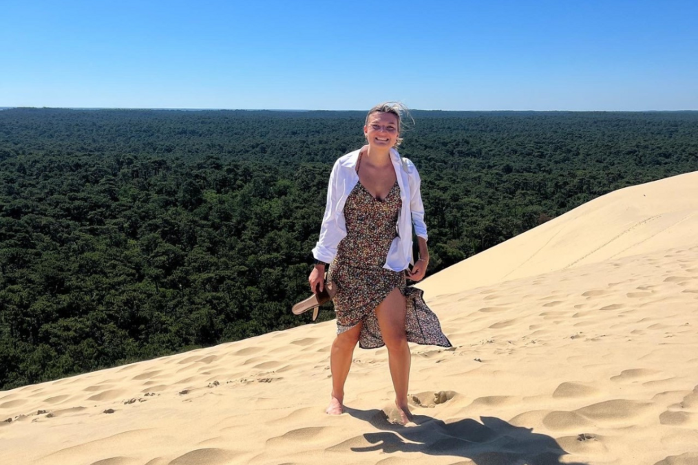 Jessica Bertolini, USAC, France: Pau - French Language and European Studies alum Jessica Bertolini standing in the sand on the beach wearing a dress and a white cardigan with blonde hair